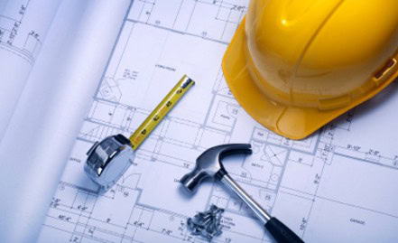 Construction tools including a yellow hard hat, hammer, tape measure, and blueprint on a work table.